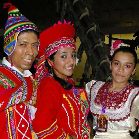 Two smiling couples in vibrant and colorful Peruvian dresses, vest, capes and hats pose in front of the Peabody dinosaurs.