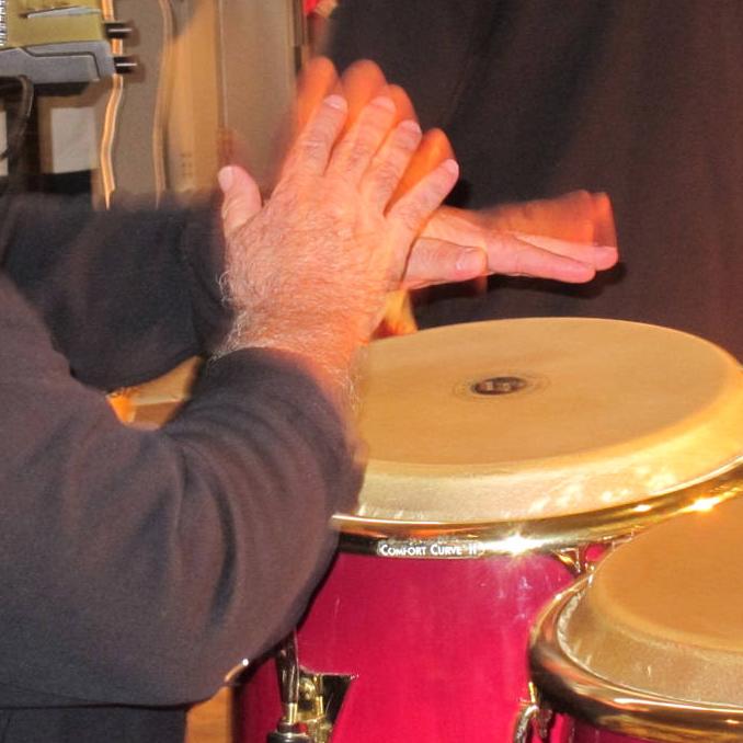 A man plays a set of red conga drums with a performance group.